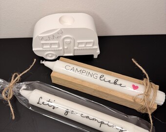 May include: White ceramic campervan candle holder with a matching candle and a candle with the text "Camping Liebe". Another candle in a plastic wrap has the text "Let's go camping". The candles are white.
