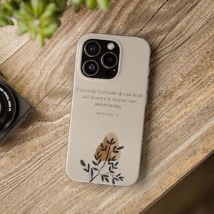 May include: A white iPhone case with a black floral design and the text "Trust in the Lord with all your heart, and do not rely on your own understanding. Proverbs 3:5".