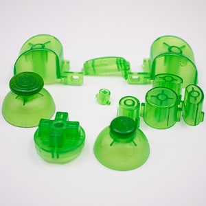 May include: A set of green replacement buttons for a video game controller. The set includes two thumbsticks, a directional pad, four face buttons, and two shoulder buttons.