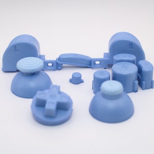 May include: A set of light blue replacement buttons for a video game controller. The set includes two analog stick caps, two shoulder buttons, four face buttons, and a D-pad.