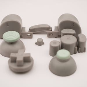 May include: A set of replacement buttons for a video game controller. The buttons are gray and have various shapes, including round, square, and rectangular. The buttons are labeled with letters, including "L", "R", "A", "B", and "Z".