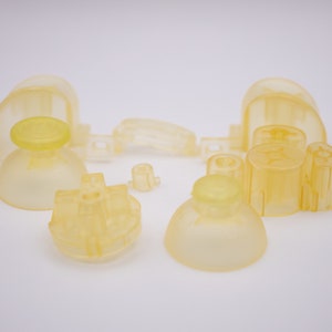 May include: A set of translucent yellow replacement parts for a video game controller. The set includes a joystick, a directional pad, and several buttons.