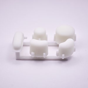 May include: A set of six white plastic components, likely for a device or product assembly, arranged on a white support structure. The shapes include rounded and rectangular forms, all in a clean, minimalist style.