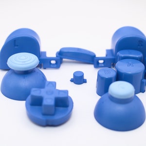 May include: A set of blue replacement buttons for a video game controller. The set includes two analog sticks, a D-pad, four face buttons, two shoulder buttons, and a start button.