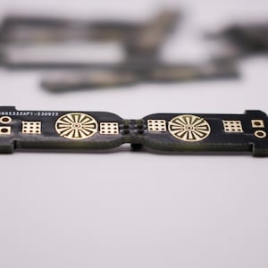May include: A black circuit board with gold-coloured markings. The board has a circular design on each end and the text "6602333AP1-230922" printed on the top.
