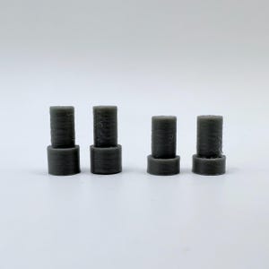 May include: Four gray plastic cylindrical spacers, each with a smaller cylinder stacked on top.