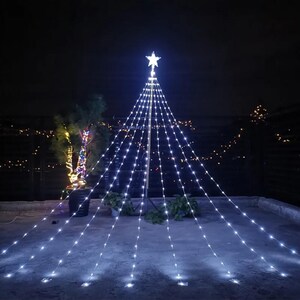 Puede incluir: Una exhibición de luces en forma de árbol de Navidad contra un cielo nocturno oscuro. El árbol está formado por hilos de luces blancas que irradian de una estrella. Las luces están dispuestas para parecerse a un árbol de Navidad.