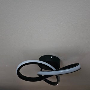 Puede incluir: Una lámpara de techo moderna con un marco de metal negro y luces LED blancas. La lámpara está diseñada en forma circular con un giro.