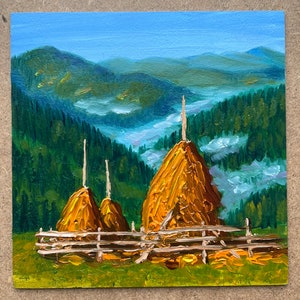 May include: A painting depicting three haystacks in a field, with a mountain range in the background. The haystacks are brown, while the mountains are blue and green. The sky is blue with clouds in the distance.