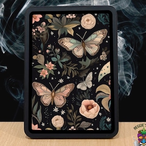 May include: A black framed square print with a floral pattern featuring butterflies and stars. The print has a dark background with pink, white, and green flowers and butterflies.