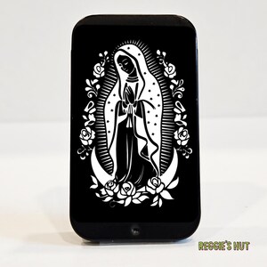 May include: Black rectangular phone case featuring a white graphic of a religious figure with hands clasped in prayer, surrounded by a floral and crescent moon design. The text "REGGIE'S HUT" is at the bottom.