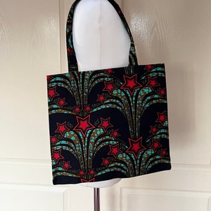 May include: A black tote bag with a colourful African print featuring red stars and teal blue accents. The bag has two long handles.