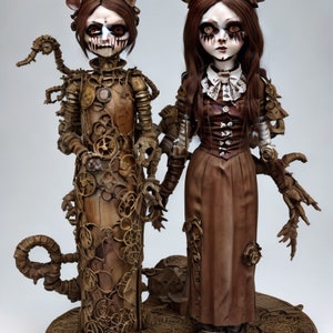 May include: Two steampunk-inspired dolls with pale skin, dark eye makeup, and eerie expressions. One doll is adorned with gears and mechanical elements, while the other wears a brown dress with a white collar. Both dolls have dark hair and are holding hands.