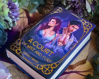 May include: A blue hardcover book with gold lettering titled "A Court of Mist and Fury" by Sarah J. Maas. The cover features a fantasy illustration of a woman and a man.