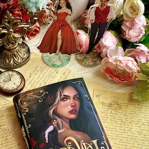 May include: A hardcover book titled "Caraval" by Stephanie Garber. The cover features a woman with long dark hair and a man in a suit. The background is a dark, ornate design with a pocket watch.