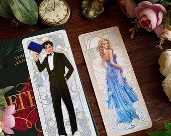 May include: Two decorative bookmarks with an art deco design. One bookmark features a man in a tuxedo holding a top hat. The other bookmark features a woman in a blue gown with butterflies. Both bookmarks have a gold and white background.