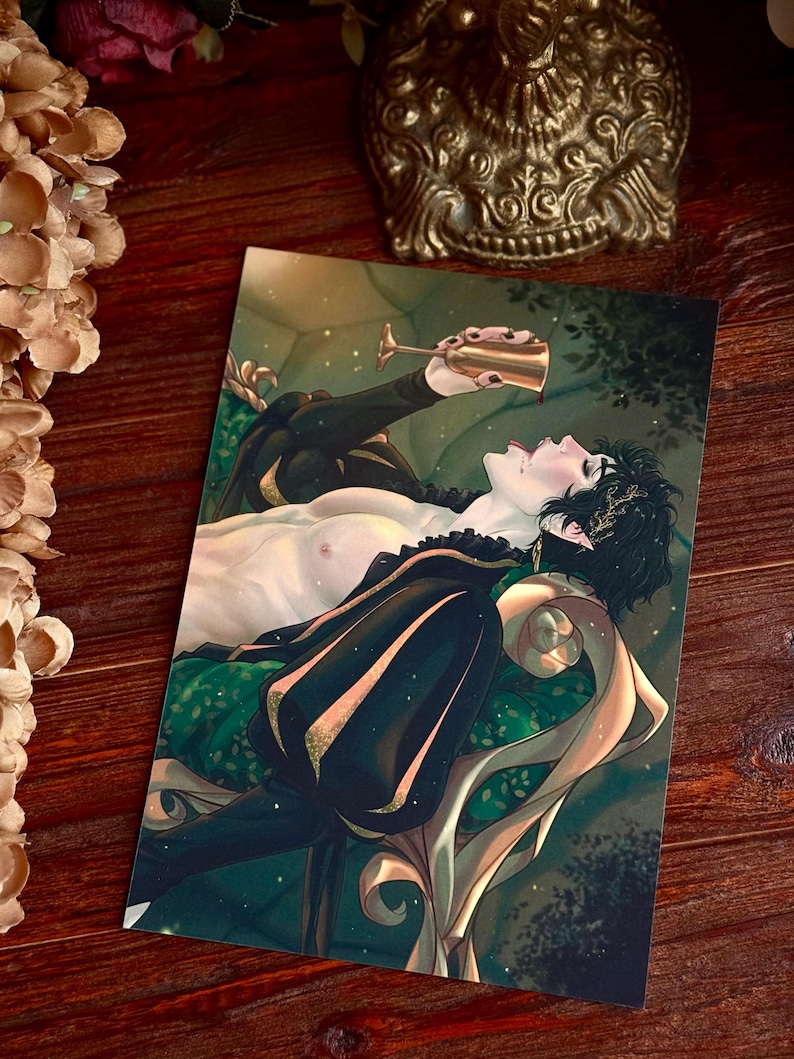 May include: Art print featuring a stylized illustration of a person reclining and drinking from a gold goblet. The person is wearing a black outfit with gold accents, and is lying on a green and gold patterned surface.