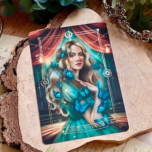 May include: A tarot card illustration depicting the Queen of Wands. The Queen is a woman with long blonde hair and a green dress. She is surrounded by blue butterflies and a red and gold tent.