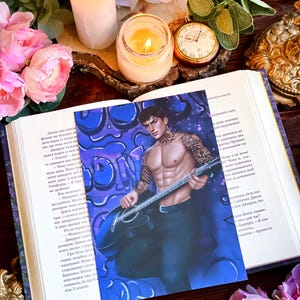 Peut inclure: Un homme tatoué joue de la guitare électrique noire. Il porte une chemise noire et un pantalon noir. L'arrière-plan est un mur de graffitis bleu et violet.