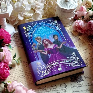 May include: A purple hardcover book titled "Once Upon a Broken Heart" by Stephanie Garber. The cover features illustrations of three characters. The background includes flowers and antique paper.