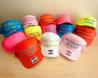May include: A collection of ten colourful trucker hats with various phrases printed on them in neon colours. The phrases include "I'm fine it's just my RBF", "I shaved my bush for this", "I'd rather go home than go big", "Dibs on the redhead", "Hoochie daddy hunting", "I put the hot in psychotic", "I'm cool but I cry a lot", "Feral but friendly", "Sorry if that was weird. It'll probably happen again", and "Blink if you want me."