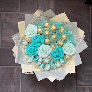 Puede incluir: Un ramo de rosas falsas de color turquesa y blanco con un centro de trufas de chocolate surtidas envueltas en papel de oro.