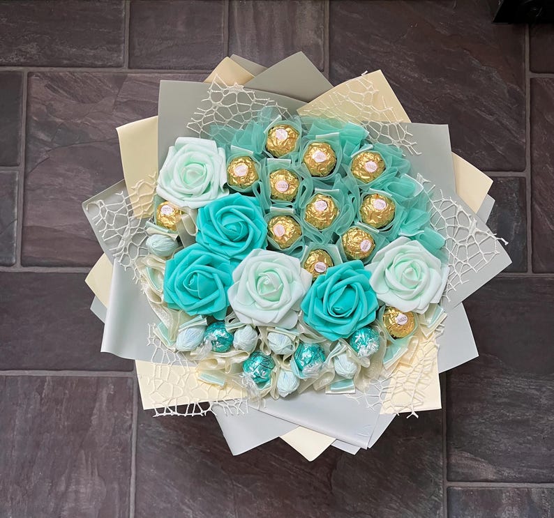 Puede incluir: Un ramo de rosas falsas de color turquesa y blanco con un centro de trufas de chocolate surtidas envueltas en papel de oro.