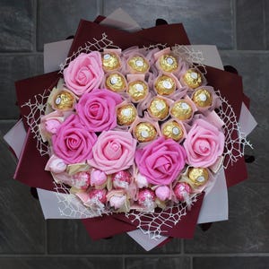 Puede incluir: Un ramo de rosas rosas y trufas de chocolate envueltas en papel burdeos y una red blanca.
