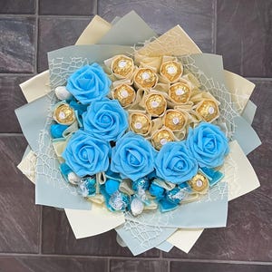 Puede incluir: Un ramo de rosas artificiales azules con un centro de chocolates envueltos en oro.
