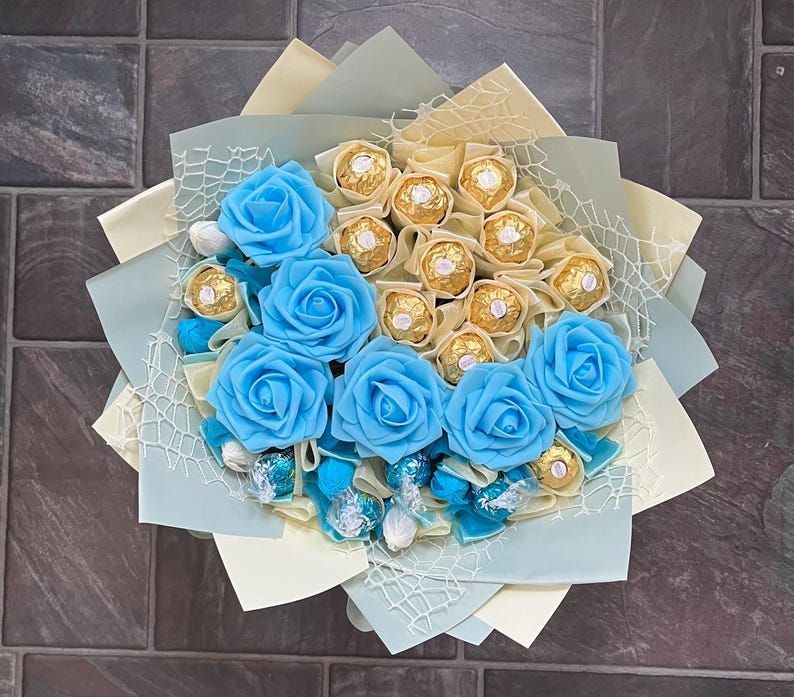 Puede incluir: Un ramo de rosas artificiales azules con un centro de chocolates envueltos en oro.