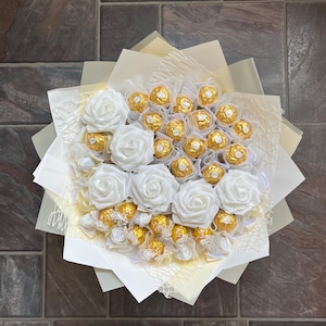 Puede incluir: Un ramo de rosas blancas de seda con un centro de chocolates envueltos en oro.