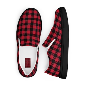 May include: Two slip-on shoes with a red and black buffalo check pattern. The shoes have a white interior and a black sole. The design is a classic, rustic style, suitable for casual wear.