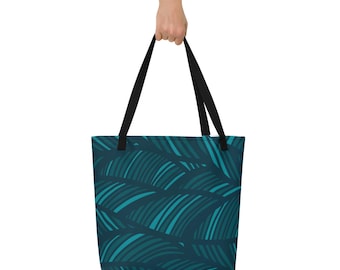 May include: A tote bag featuring a teal and dark teal leaf design. The bag has black handles and is held by a hand. The bag is made of a durable material and is suitable for carrying shopping, books, or other items.