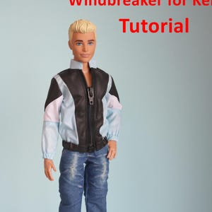 May include: A doll wearing a black, white, and light blue windbreaker jacket with a zipper, paired with blue jeans and black and white sneakers. The image has the text "Windbreaker for Ken Tutorial PDF".