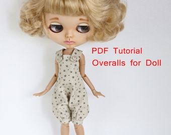 May include: A doll wearing beige overalls with a gray star pattern. The overalls have two silver buttons on the straps. The doll has blonde curly hair and large blue eyes. The text "PDF Tutorial Overalls for Doll" is written in red at the top of the image.