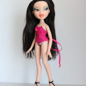 May include: A pink and black doll with long black hair wearing a pink corset and black high heels.