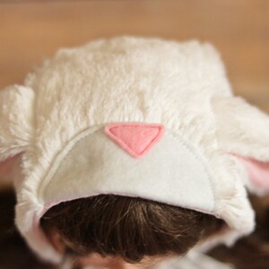 May include: White fluffy hat with pink bunny ears and a pink felt triangle on the front.