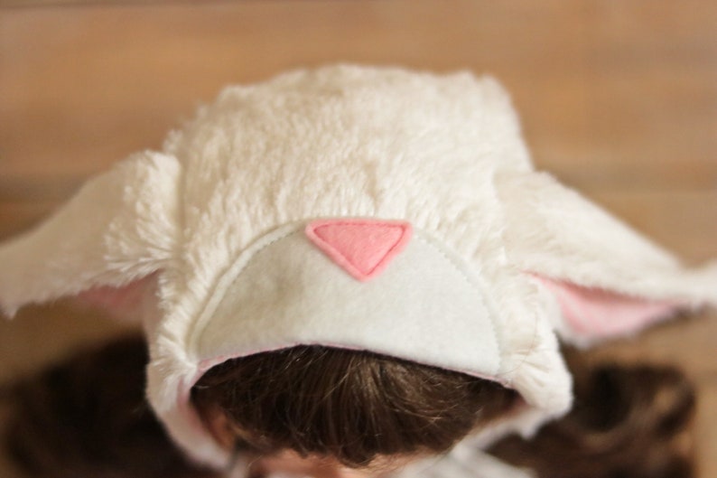 May include: White fluffy hat with pink bunny ears and a pink felt triangle on the front.