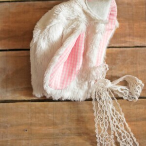 May include: White bunny hat with pink and white gingham ears and a white lace tie.