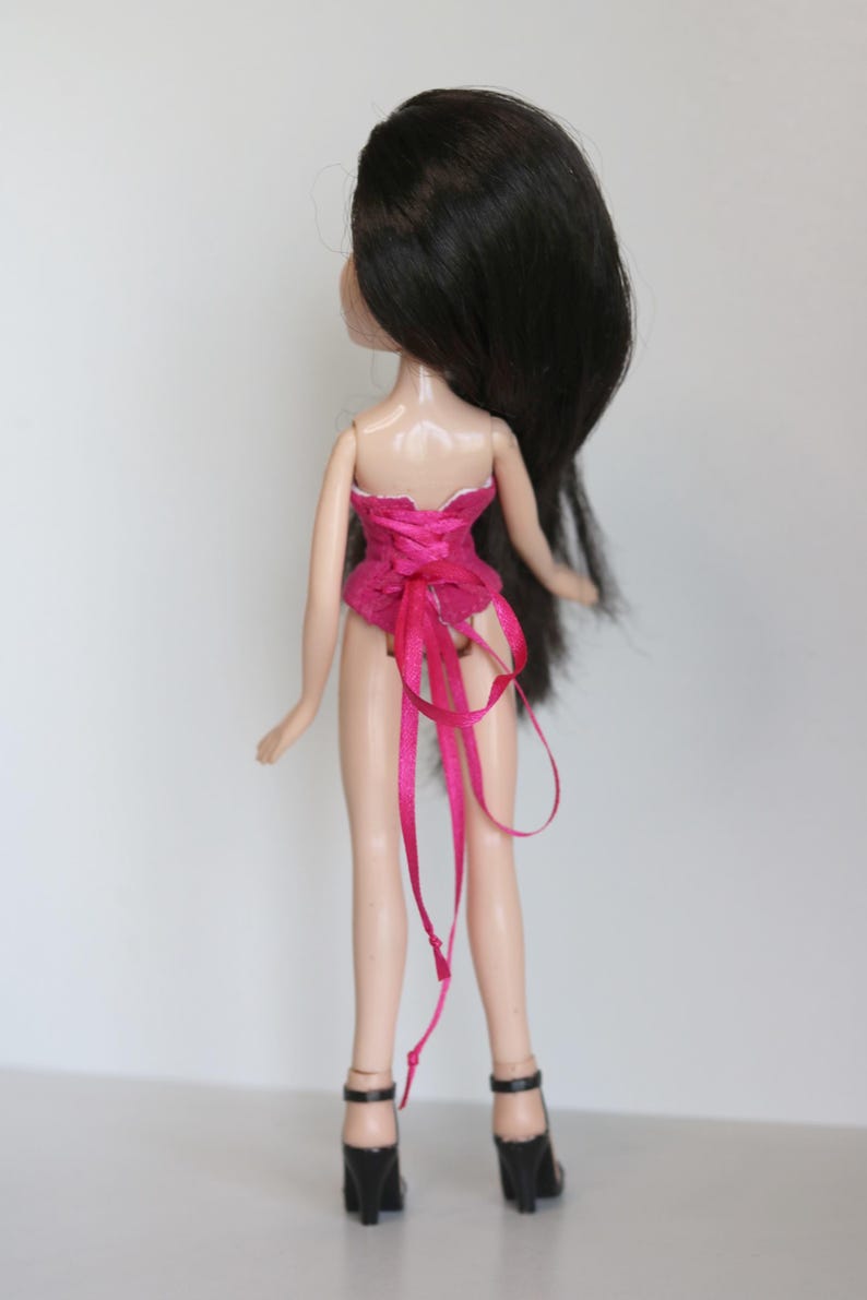May include: A pink corset with a satin ribbon tied in the back. The doll is wearing black high heels.