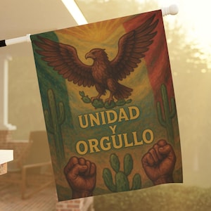 May include: A rectangular flag with a design featuring a brown eagle with outstretched wings, a cactus, and the words "UNIDAD Y ORGULLO" in gold. The flag has a green, red, and yellow background. Two fists are at the bottom.