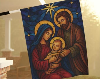 May include: A religious flag featuring a stained-glass style depiction of the Holy Family. The image shows Mary, Joseph, and baby Jesus, surrounded by a blue background with stars and a large star. The flag is mounted on a white pole.