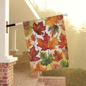 May include: A decorative fall-themed garden flag with a white background and a pattern of colorful maple leaves in shades of red, orange, yellow, and green.