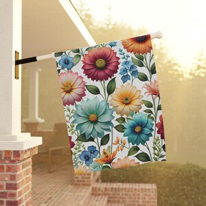May include: A colorful floral garden flag with a white background. The flag features a variety of flowers in shades of pink, blue, yellow, and red.