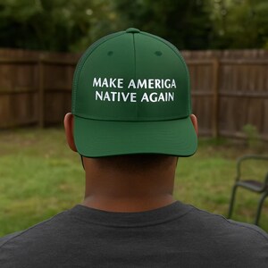 May include: A green trucker hat with the text "MAKE AMERICA NATIVE AGAIN" in white block letters. The hat has a mesh back and a curved brim. The person wearing the hat is facing away from the camera.