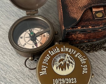 May include: A brass pocket compass with a hinged lid featuring the engraved text Paul-o inside. The exterior lid displays a mountain graphic with the text May your faith always guide you, 10/29/2023, and BJE. A brown leather case is included.