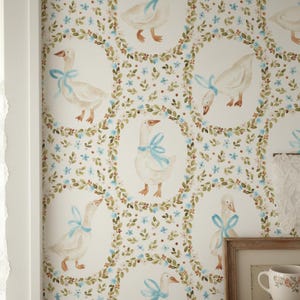 May include: Wallpaper with a repeating pattern of geese wearing blue ribbons, encircled by floral wreaths. The background is white with blue flowers and green leaves, creating a quaint, whimsical design for a room.