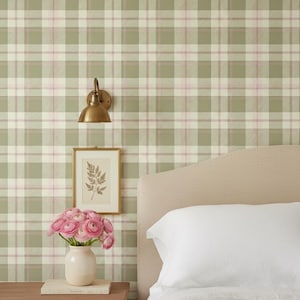 Könnte beinhalten: Ein Schlafzimmer mit grün-weiß-rosa karierter Tapete. Eine Wandleuchte aus Messing und ein gerahmter botanischer Druck hängen an der Wand. Eine Vase mit rosa Blumen steht auf einem Nachttisch neben einem Bett mit einem weißen Kissen.