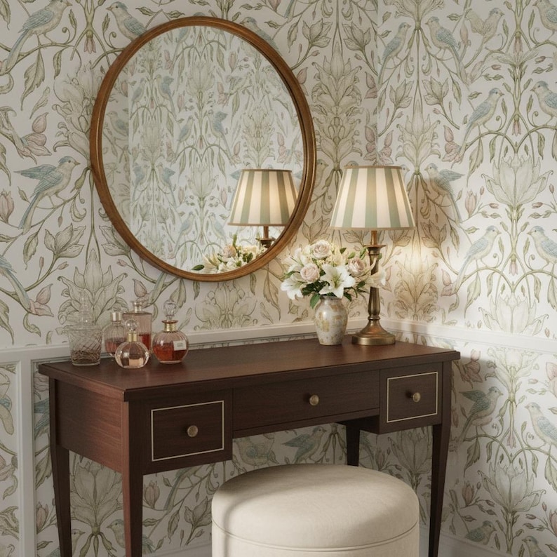 May include: A dark wood vanity table with three drawers and gold-toned knobs, paired with a round mirror in a matching wood frame. A table lamp with a striped shade and a small vase of white flowers sit on the surface, alongside three glass bottles.
