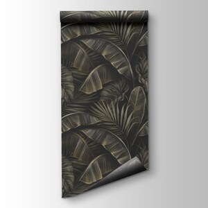 May include: A roll of wallpaper featuring a dark background with a repeating pattern of stylized tropical leaves in shades of gold and green. The leaves include banana leaves and palm fronds.